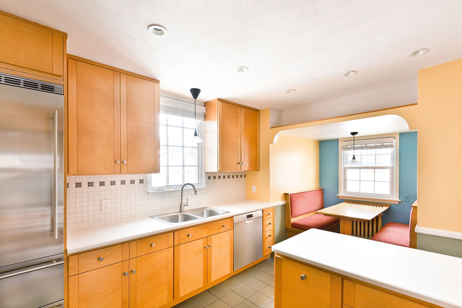 A kitchen with light wood cabinets, stainless steel appliances, and a small table in a nook.