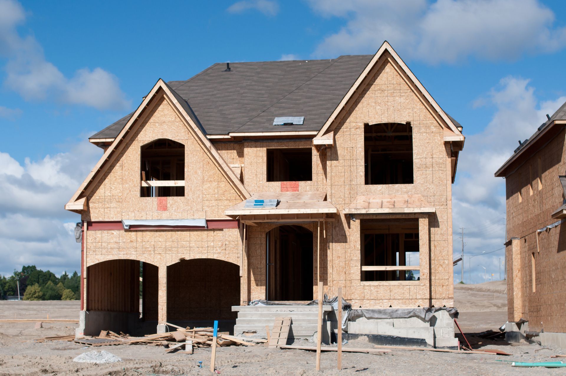 New house under construction with exposed wooden framing. Blue sky and construction materials are visible.