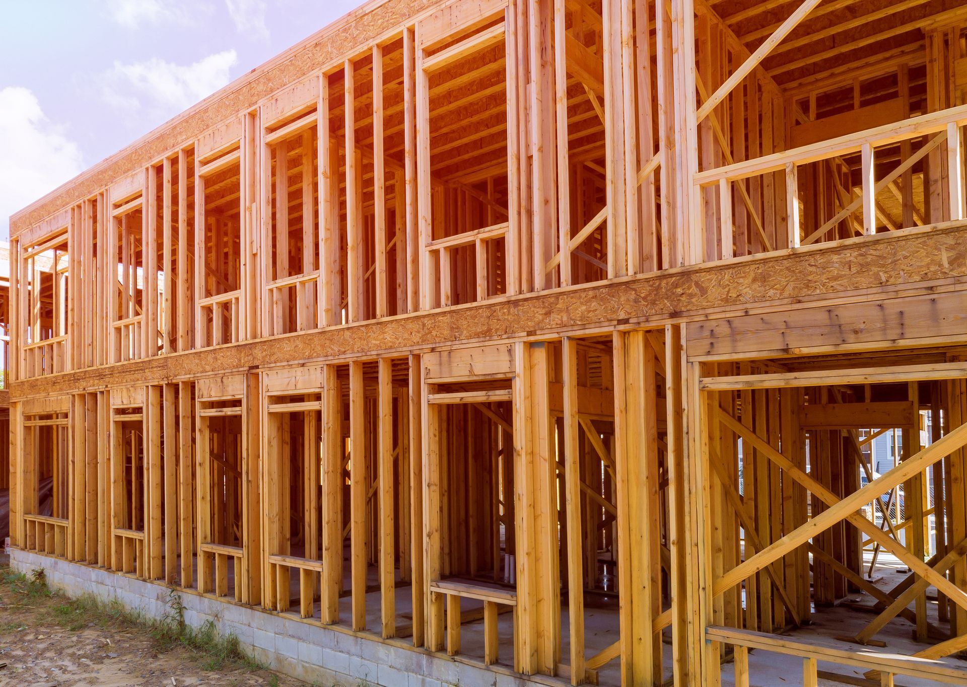 Wooden framework of a two-story building under construction; sunlight shines through.