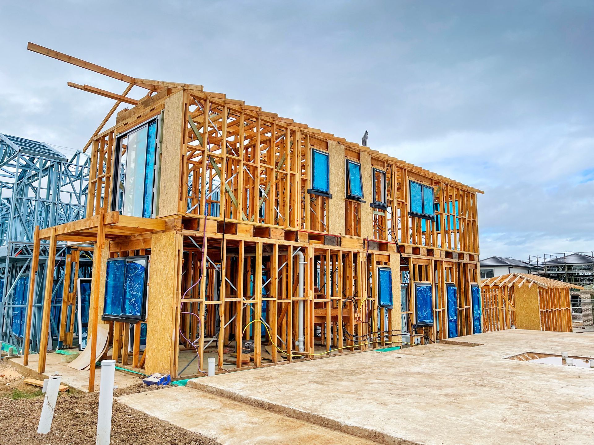 Two-story wooden house frame under construction on a concrete foundation under a cloudy sky.