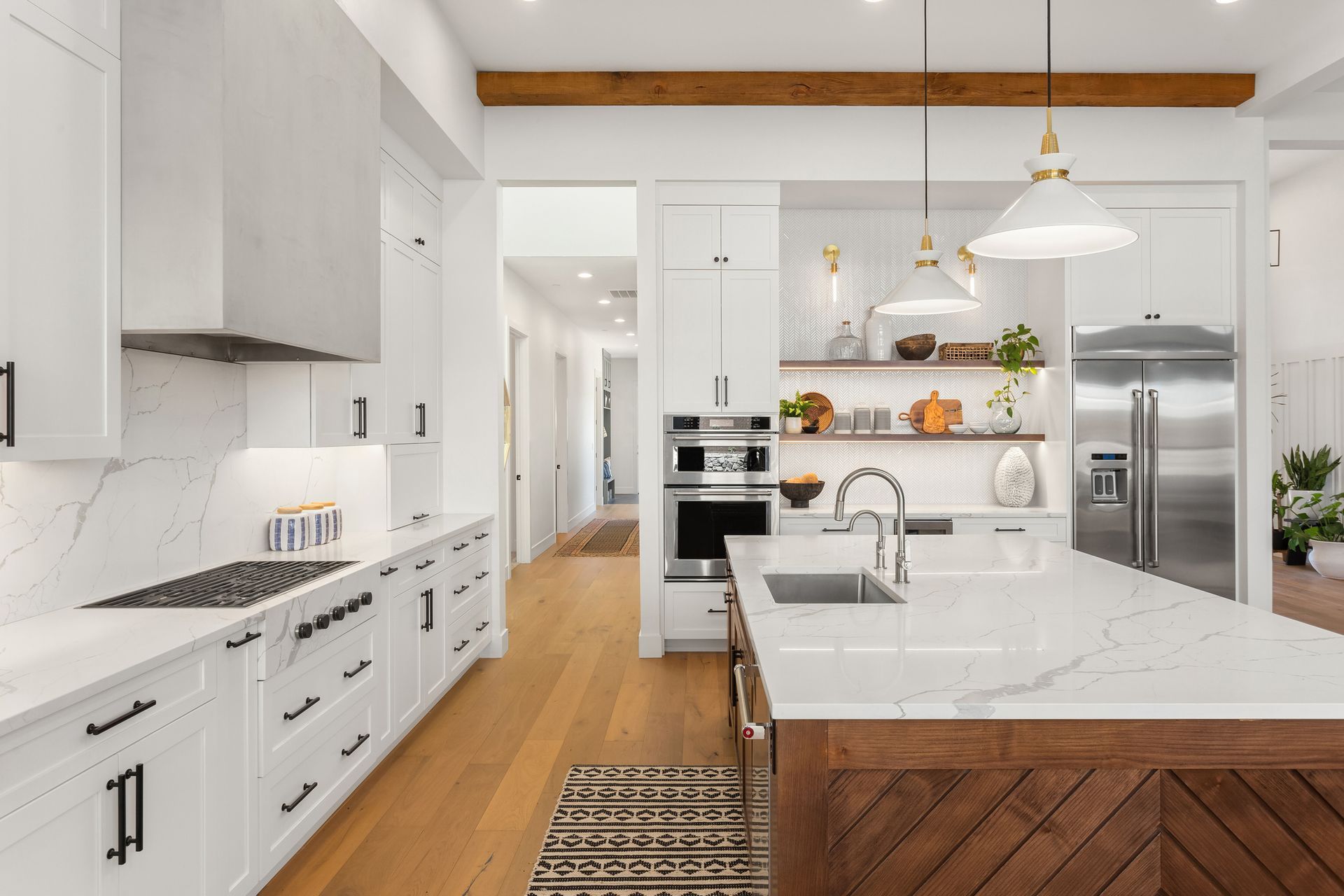 White kitchen with marble countertops, wood accents, and stainless steel appliances.