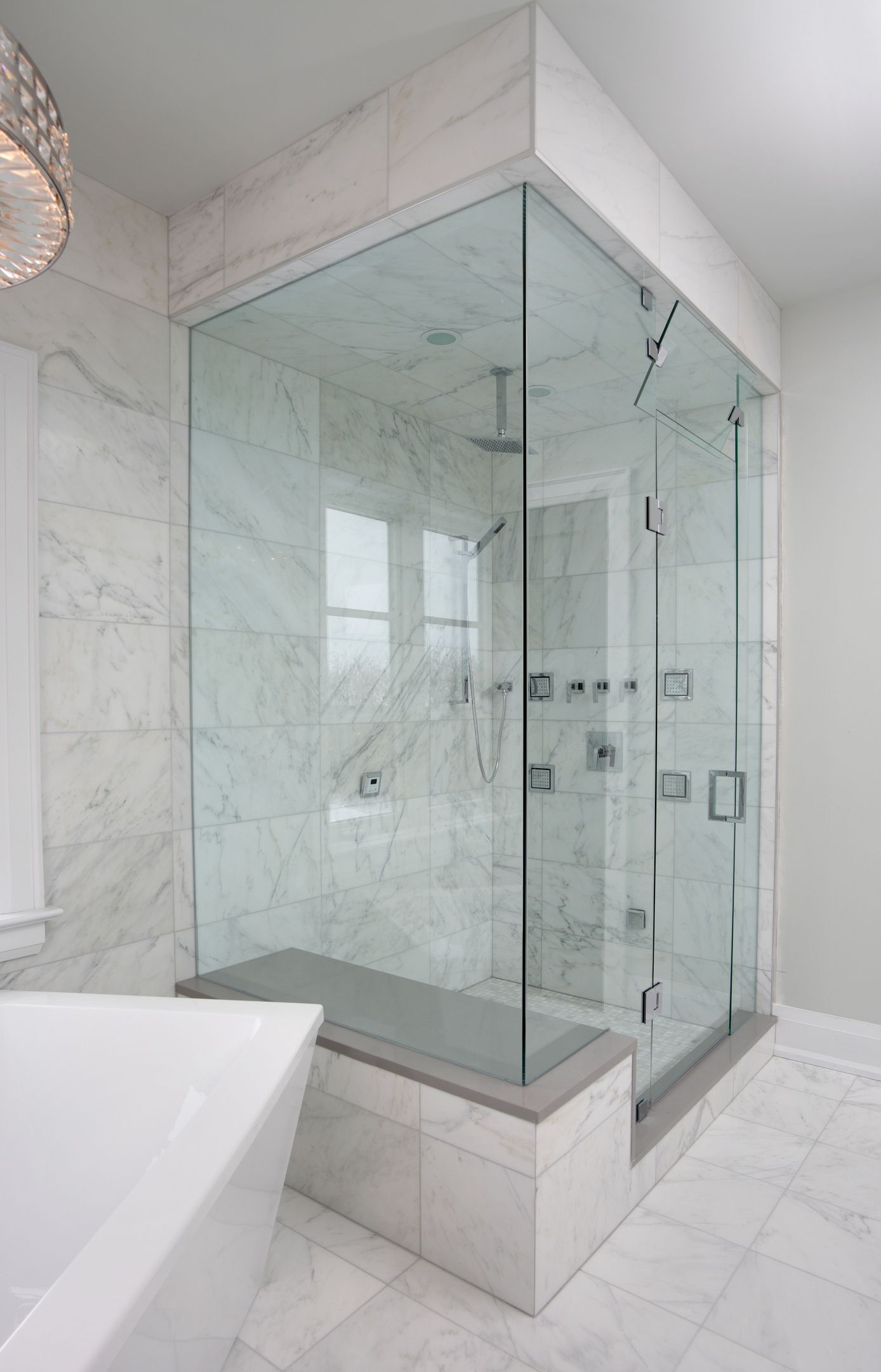 Modern glass shower enclosure with marble walls and a built-in bench.