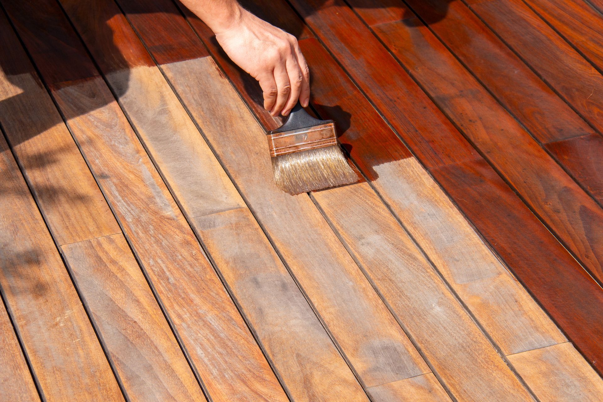 A person applying wood stain to a deck with a brush, showcasing the color difference.