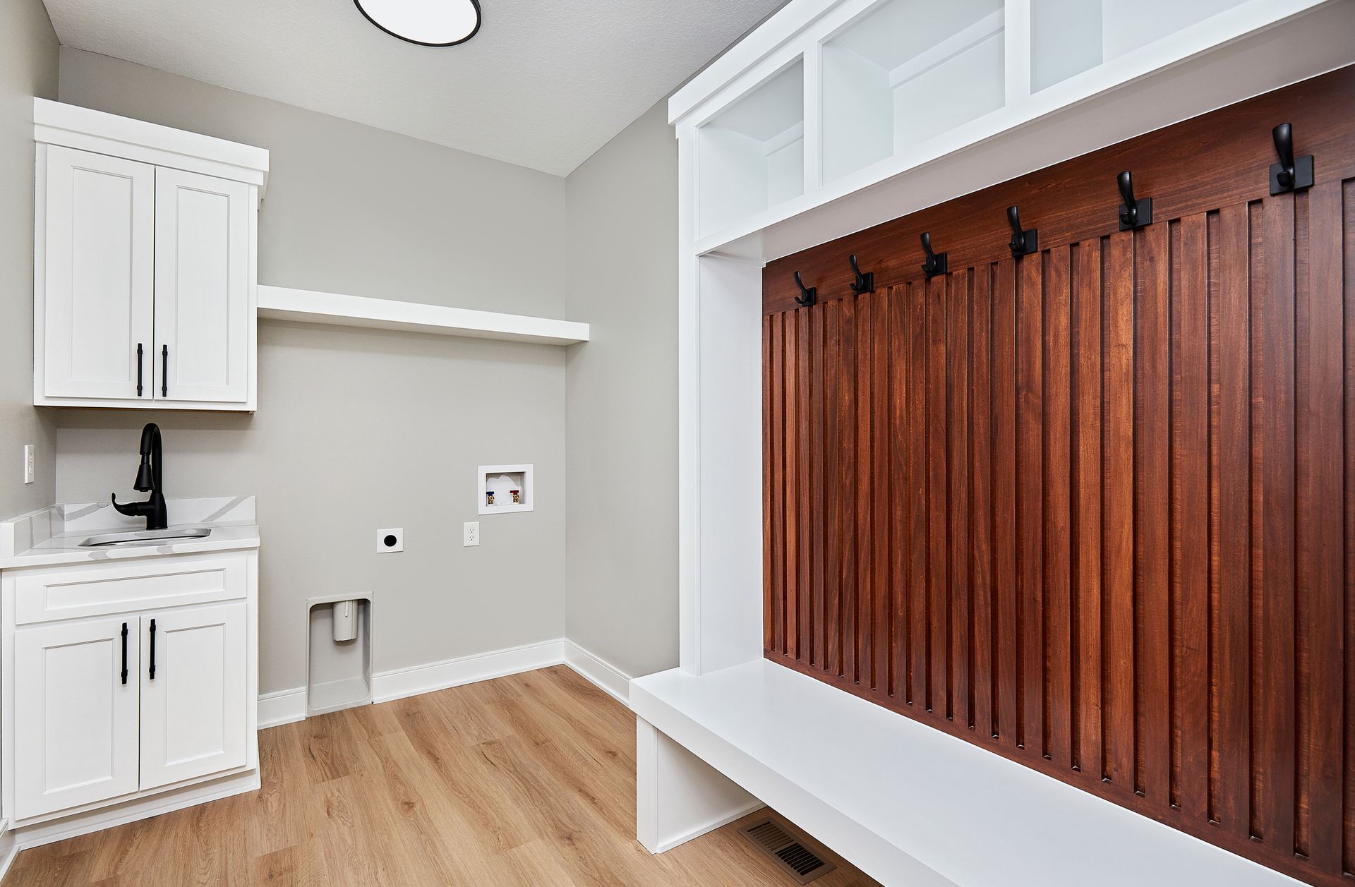 Laundry room with white cabinets, a wooden accent wall with hooks, and a bench.