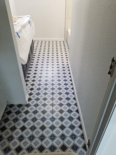 Bathroom hallway with patterned tile floor, walls, and partially visible bed.