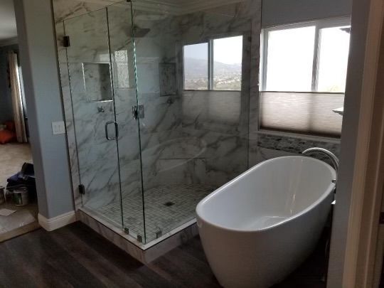 Modern bathroom with a glass shower, soaking tub, and window. Gray and white tones.