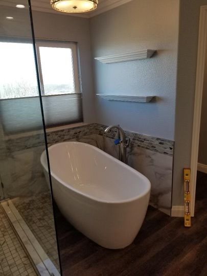 Modern bathroom with a white, oval bathtub, marble tile, and wood-look flooring.