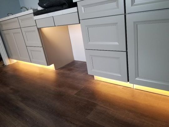 Light-colored cabinets with under-cabinet lighting installed above dark wood-look flooring.