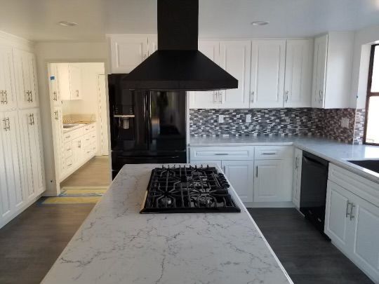 Modern white kitchen with black accents: range hood, appliances, and island with cooktop.