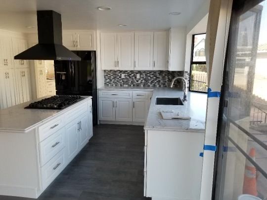 Modern white kitchen with black appliances, island, and gray flooring.