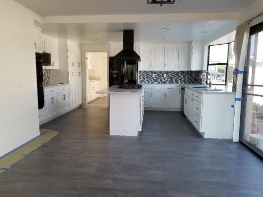 Newly renovated kitchen with white cabinets, gray flooring, and black range hood.