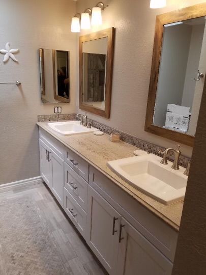 Bathroom with double vanity, white cabinets, light countertop, and wooden framed mirrors.