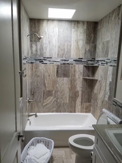 Bathroom with white tub, wood-look tile, small skylight, and a toilet.