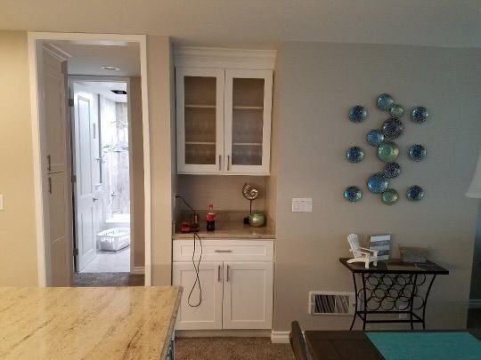A small white kitchen cabinet with glass doors next to a hallway and table against a gray wall with art.