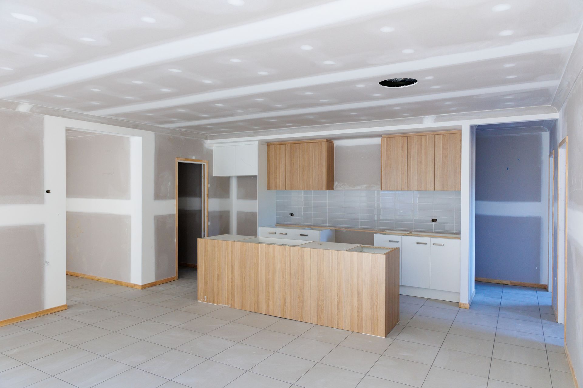 Interior view of a kitchen under construction, featuring wooden cabinetry, a central island, and exposed drywall.