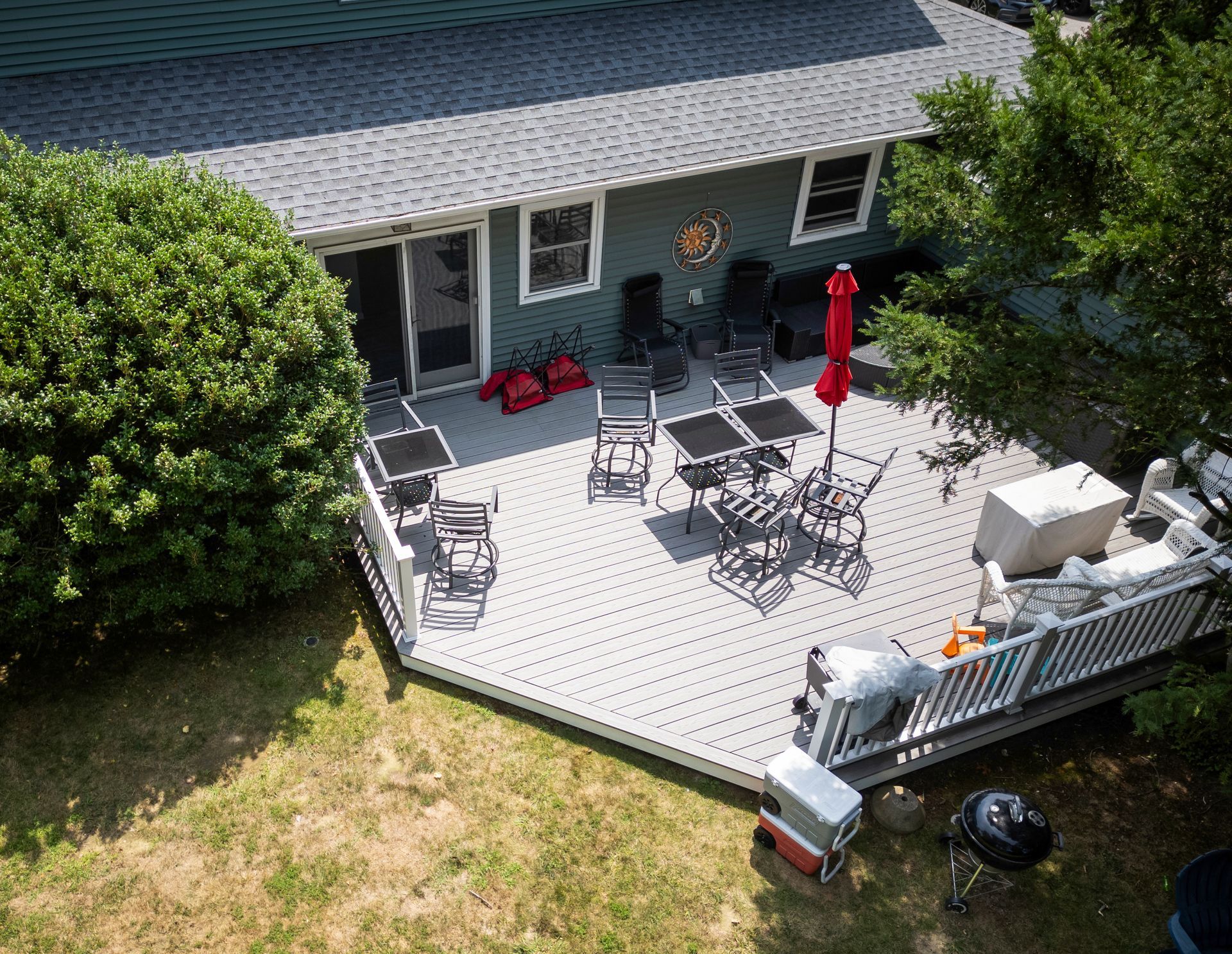 Aerial view of a deck with black tables and chairs, a red umbrella, and a green house.