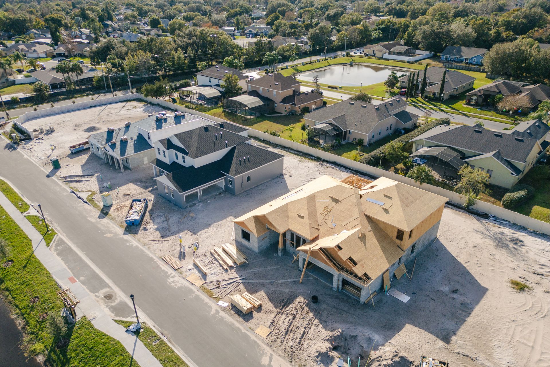 Aerial view of new homes under construction in a neighborhood with surrounding houses and a pond.