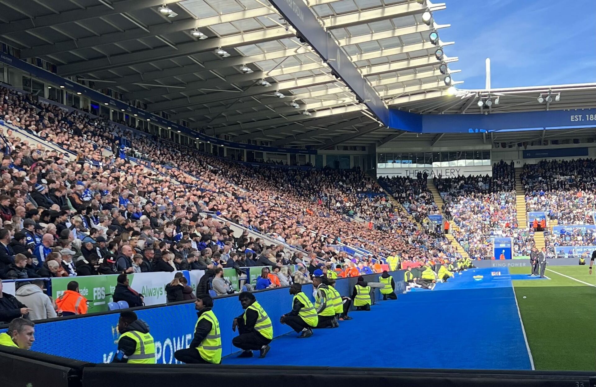a group of people are kneeling on the sidelines of a football stadium .