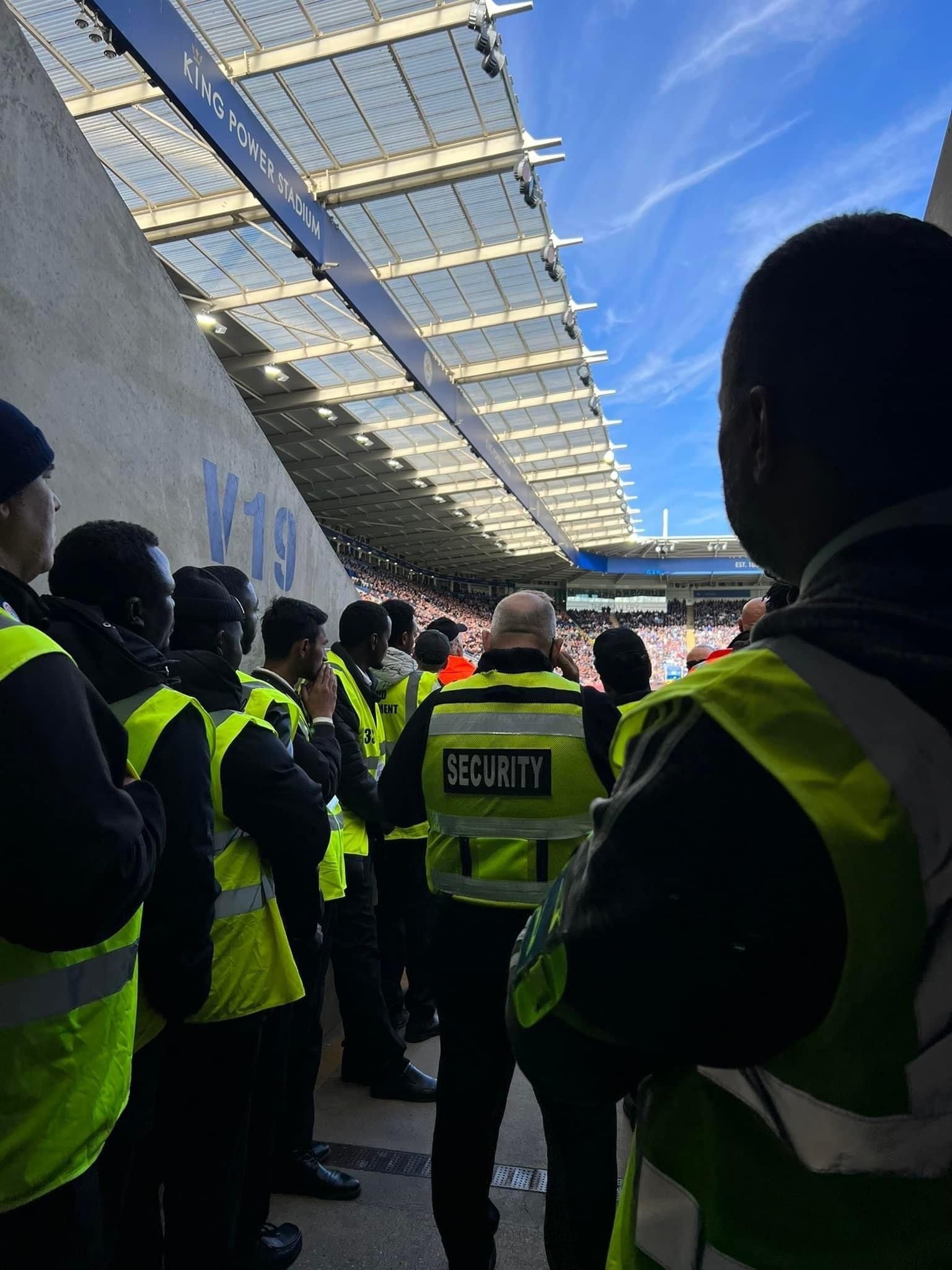 A group of men in yellow vests are standing in front of a stadium.