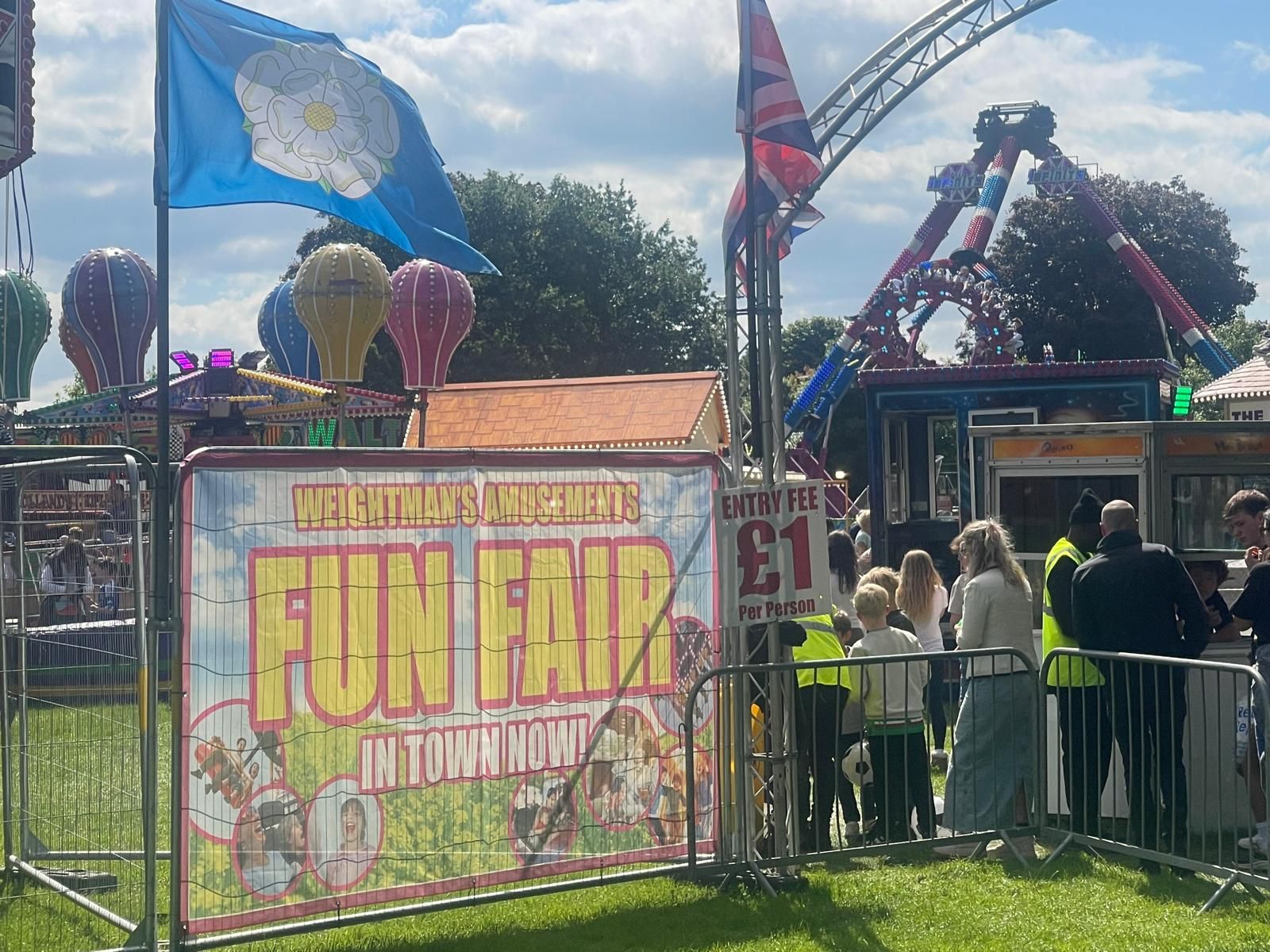 A group of people are standing in front of a fun fair sign.