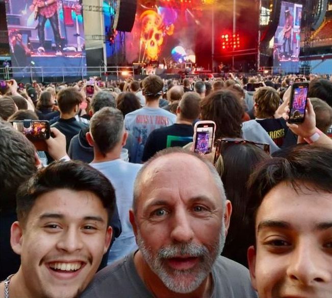 A man wearing a t-shirt that says rusty chains stands in front of a crowd at a concert