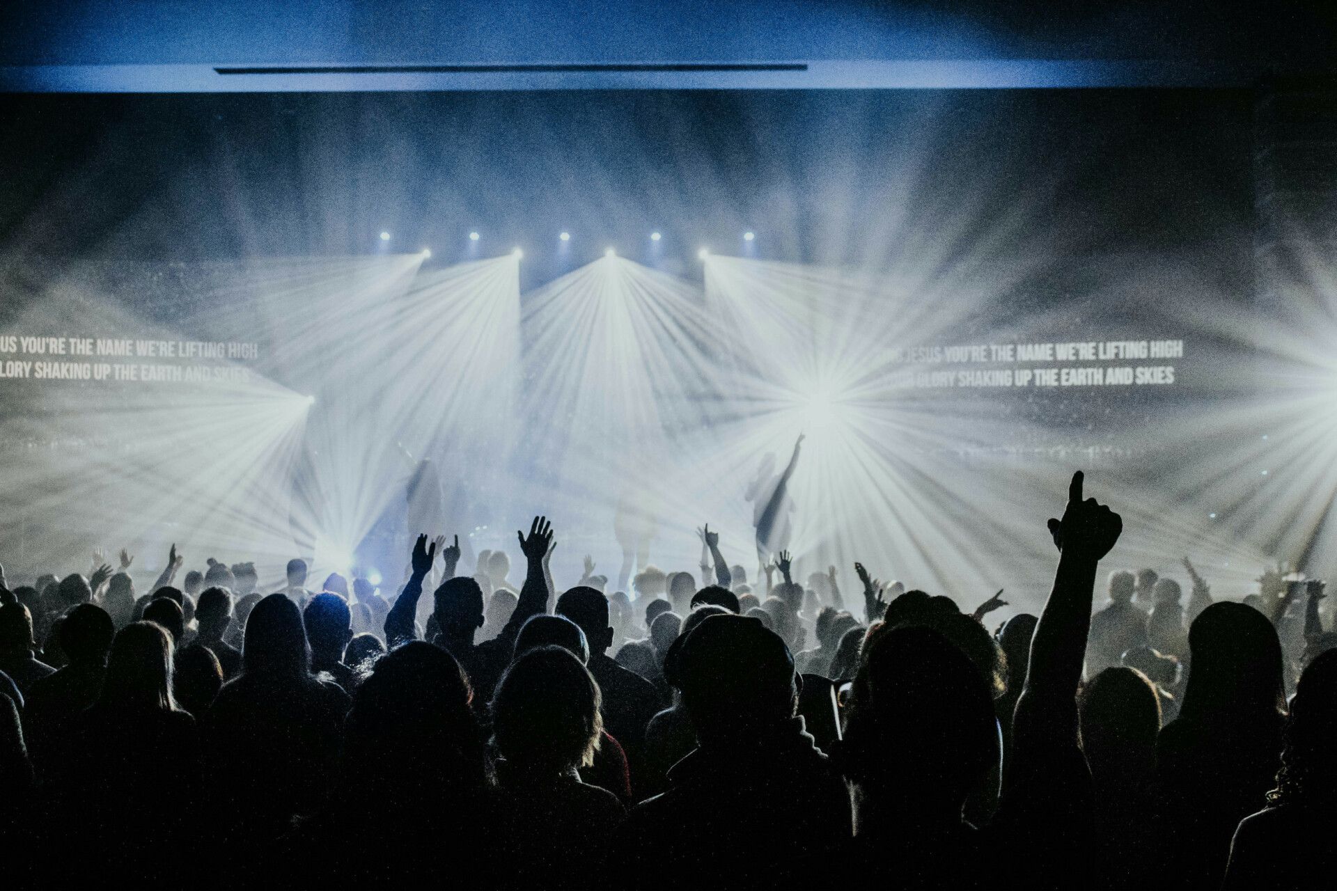 A crowd of people are standing in front of a stage with their arms in the air.