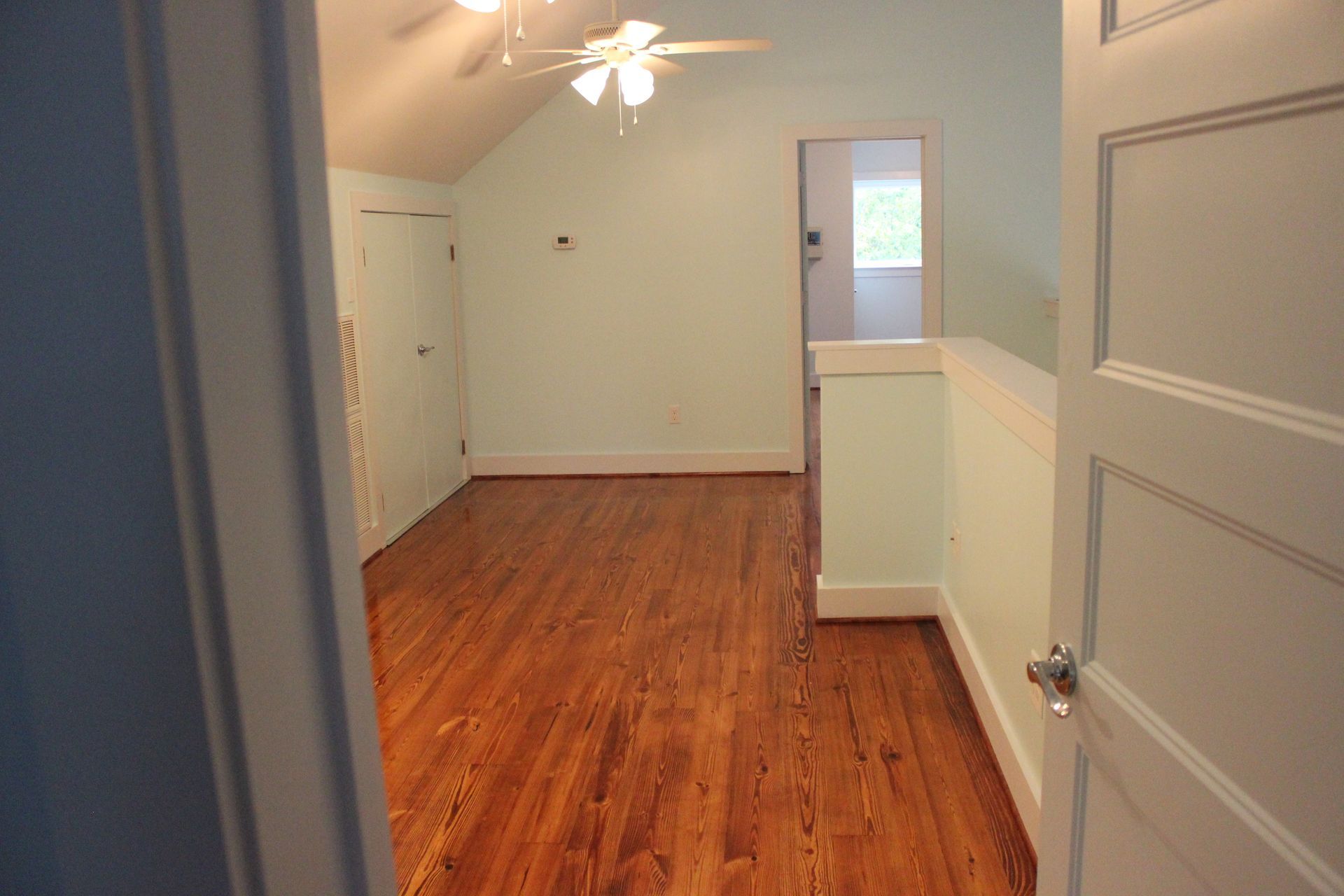 A hallway with hardwood floors and a ceiling fan in a house.