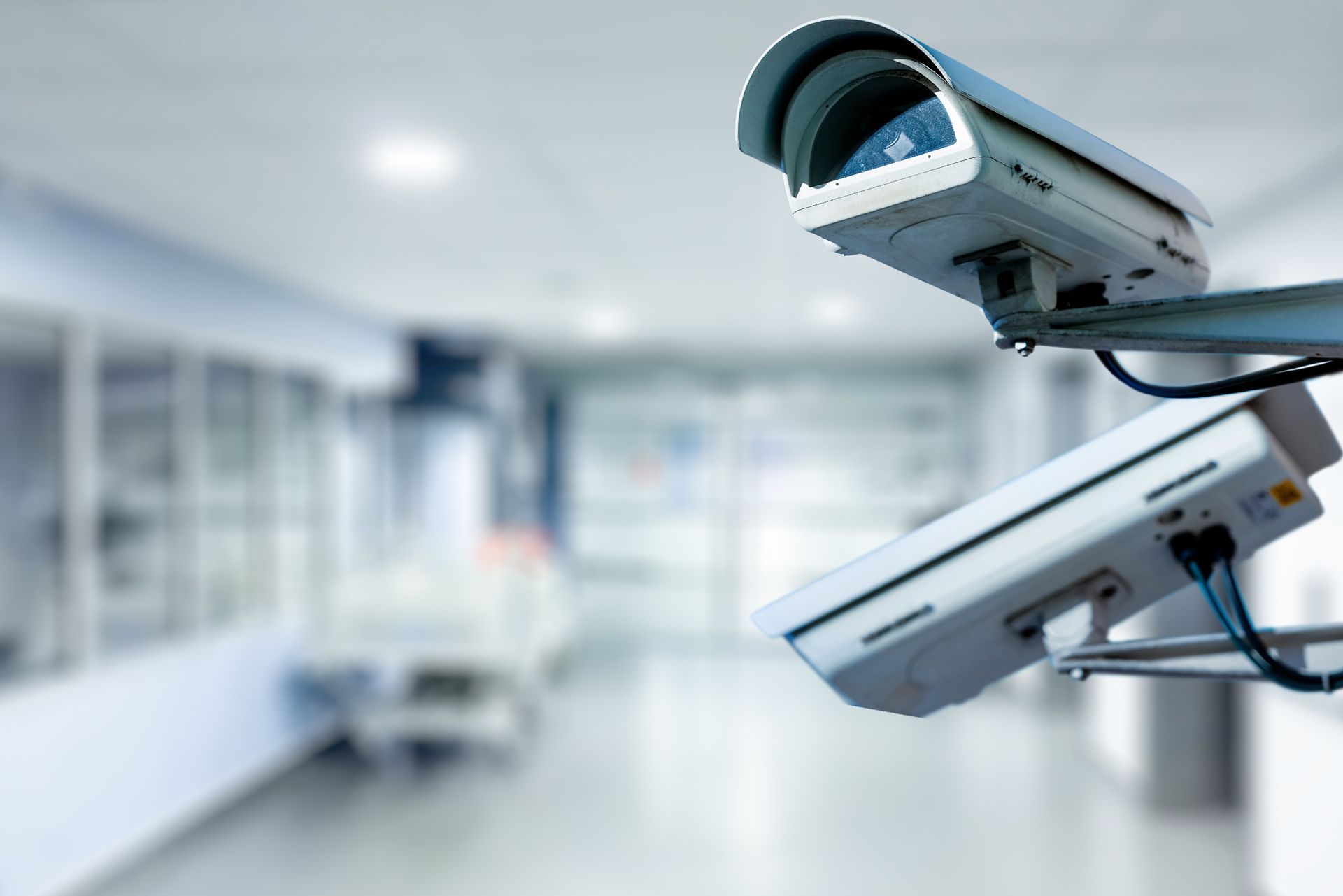 Two security cameras mounted; blurry hospital corridor background.
