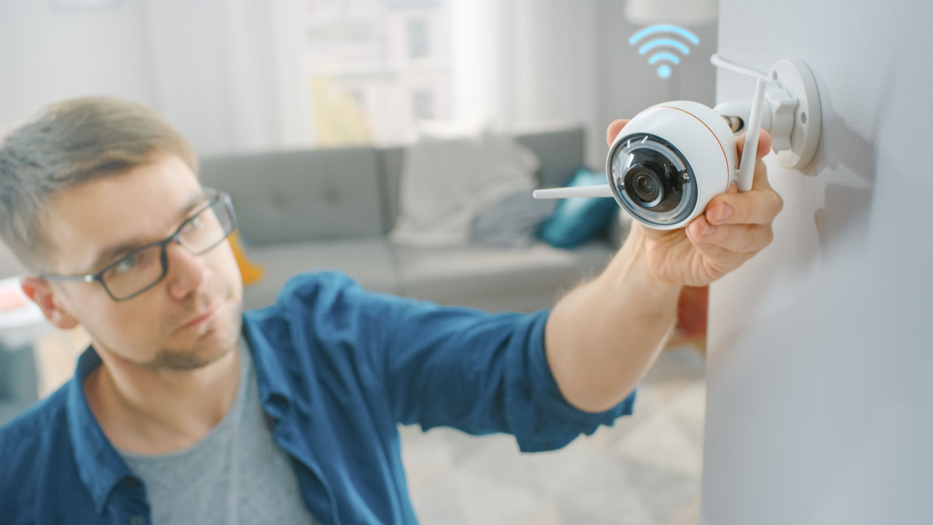Man installing a white security camera on a wall; indoor, wi-fi signal above.