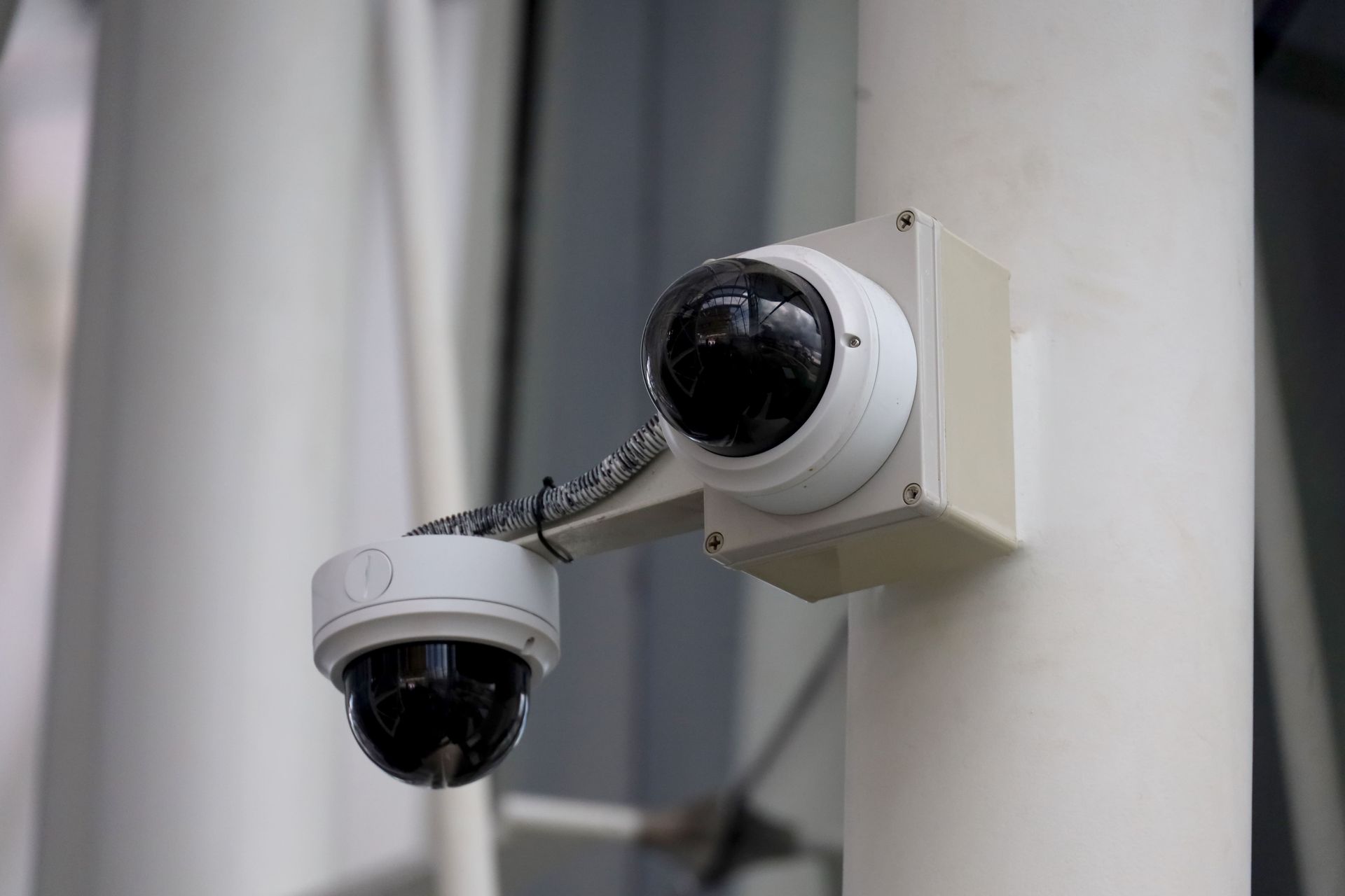 Two white dome security cameras mounted on a white pole, cables visible.