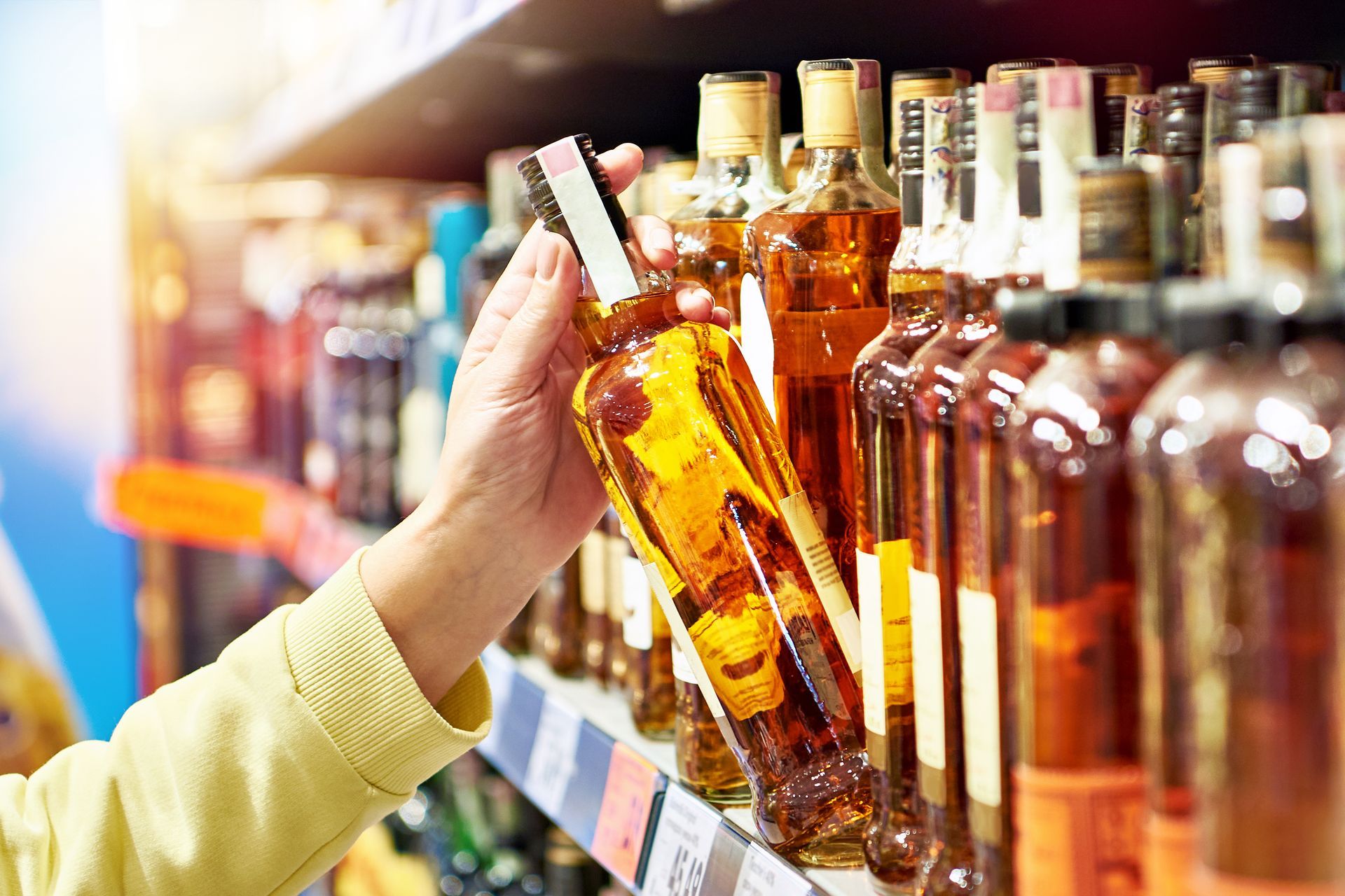 Hand pulling a liquor bottle off of a shelf in a liquor store. Learn more about The Beach Bucket's adult beverages options.