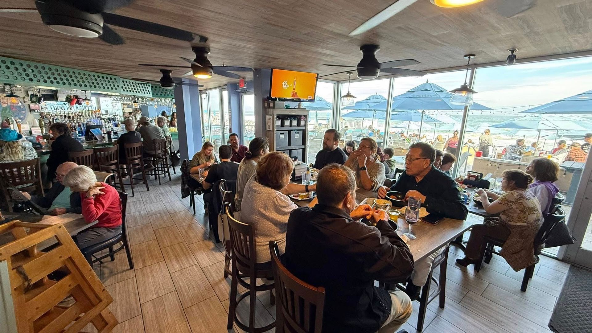 Interior of a restaurant with people seated at tables, beach views outside.