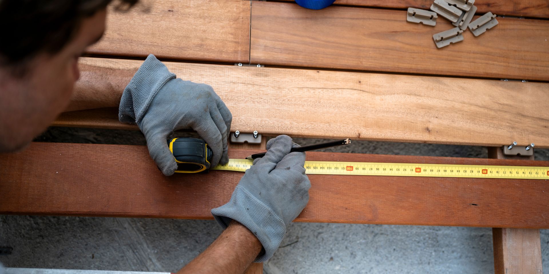 Contractor measuring and installing wood deck boards with tools during railing or deck construction 