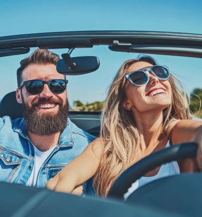 A man and woman smiling while sitting in a car wearing sunglasses