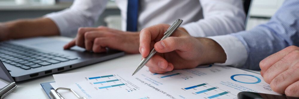 A Man Is Writing On A Piece Of Paper While Another Man Is Using A Laptop — Visionary Accounting In Parkes, NSW