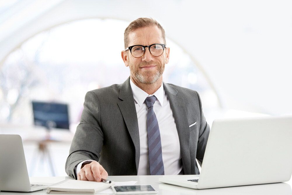 A Man In A Suit And Tie Is Sitting At A Desk With A Laptop — Visionary Accounting In Dubbo, NSW