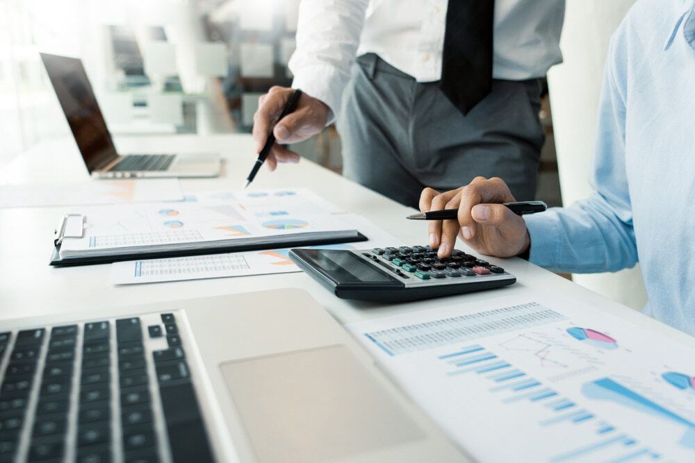 Two Men Are Sitting At A Table With A Laptop And A Calculator — Visionary Accounting In Forbes, NSW