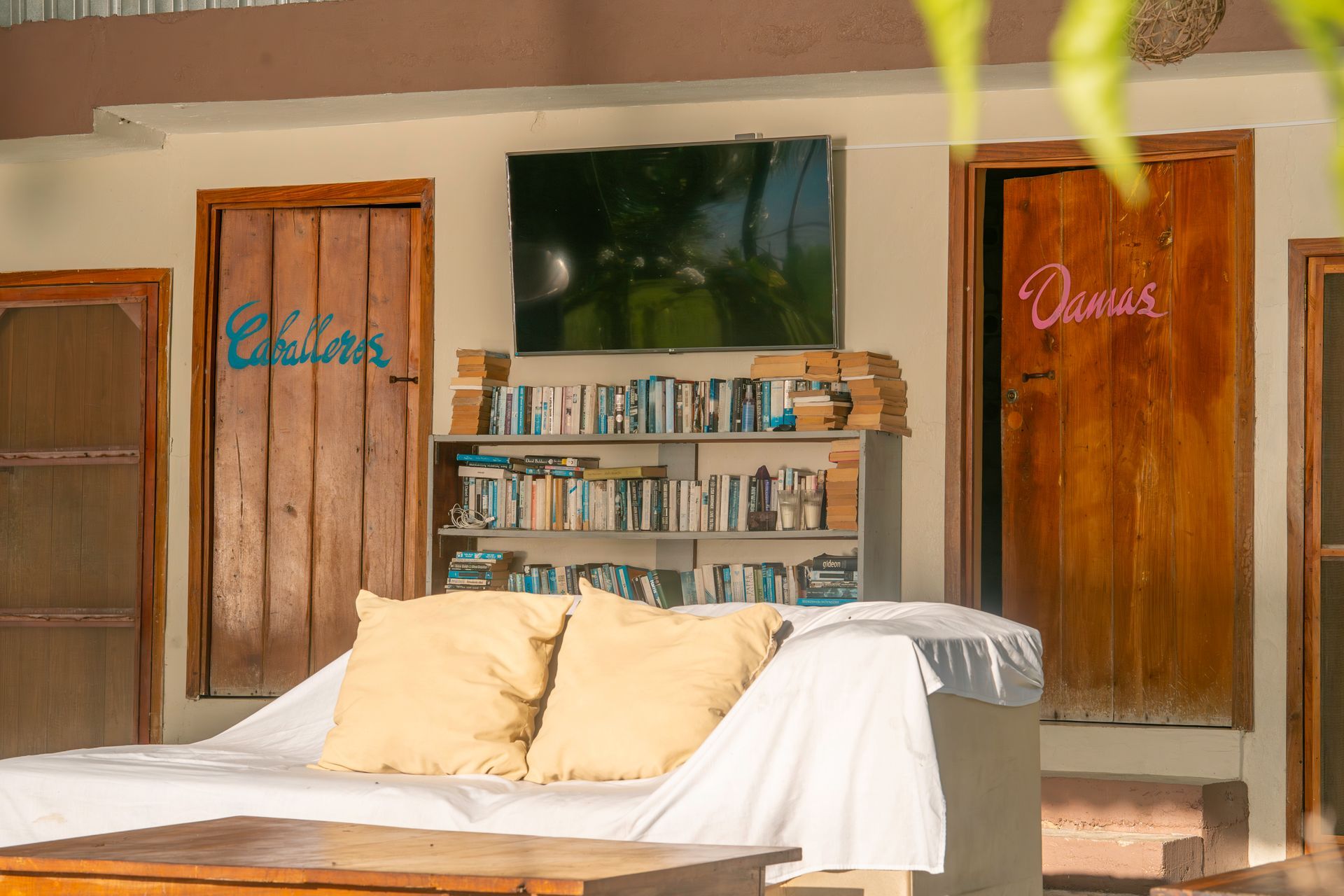 Una acogedora sala de estar con un sofá con dos cojines beige, una estantería, un televisor y puertas de madera con letreros con texto.