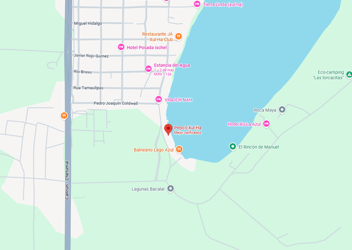 Un mapa digital que muestra un marcador rojo que indica la ubicación de un negocio junto a un lago, rodeado de calles y otros puntos de referencia locales.