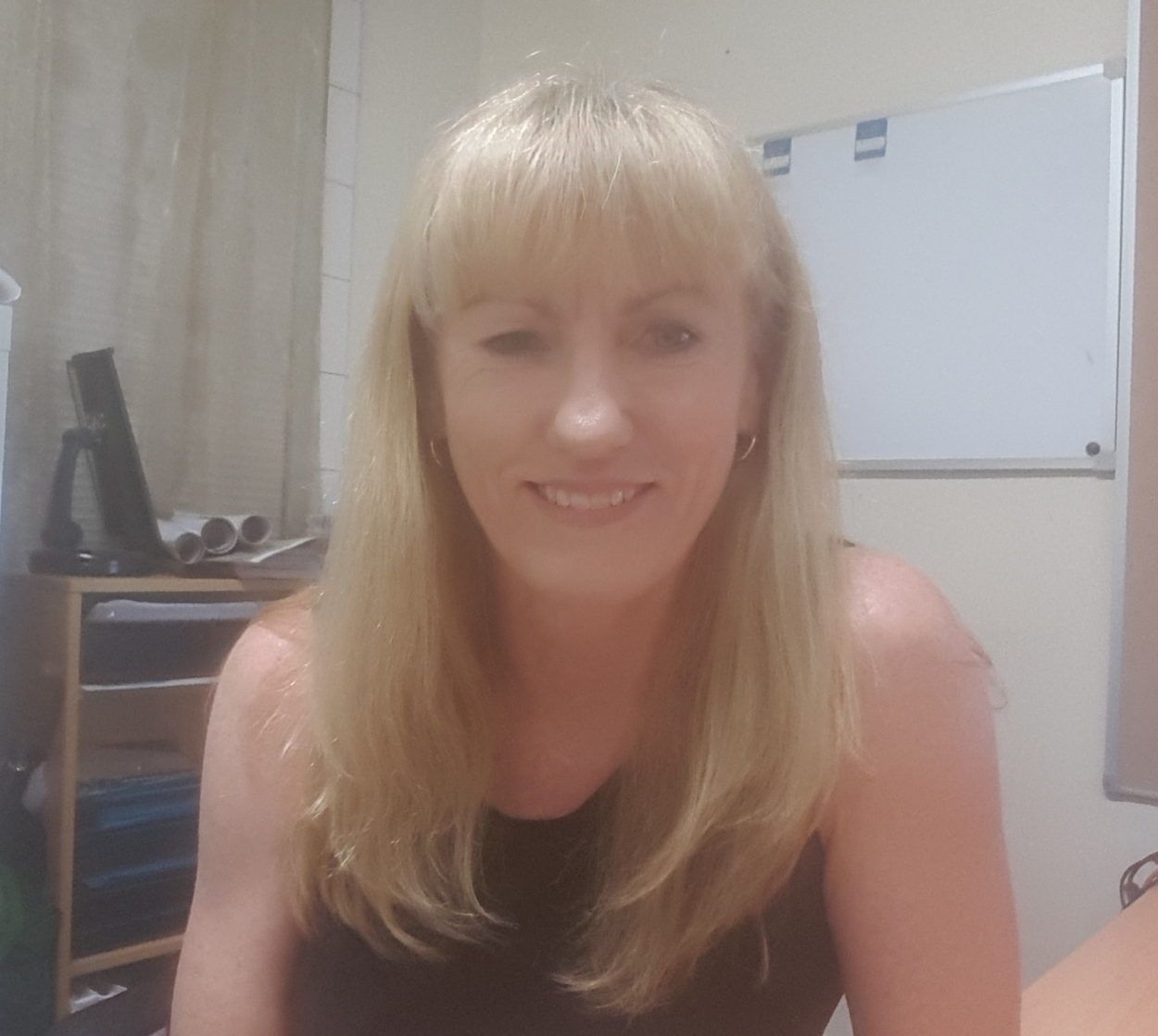 Woman with blonde hair and bangs, smiling, in an office setting.