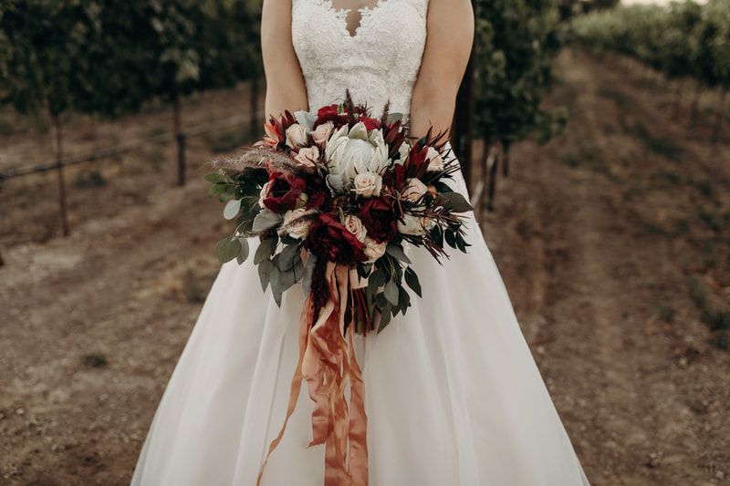 A bride in a wedding dress is holding a bouquet of flowers in a vineyard.