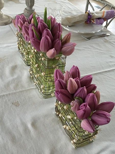 Three vases filled with purple flowers and pearls on a table