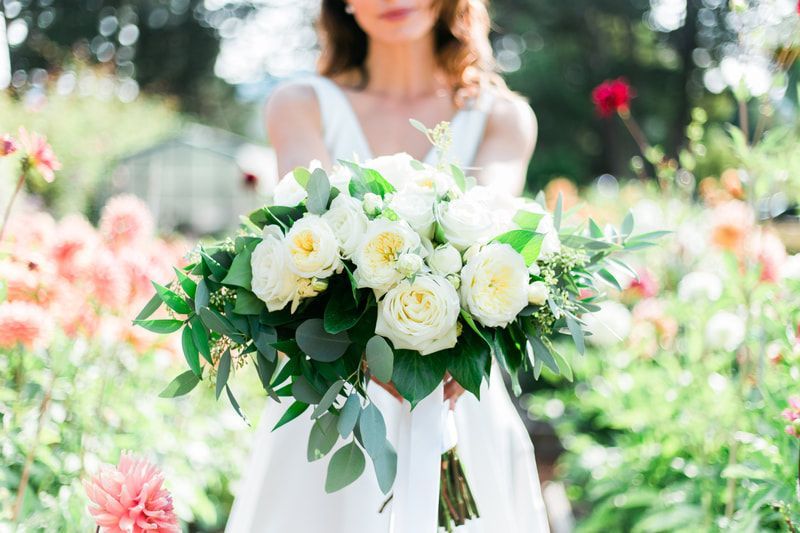 A bride in a white dress is holding a bouquet of white flowers.