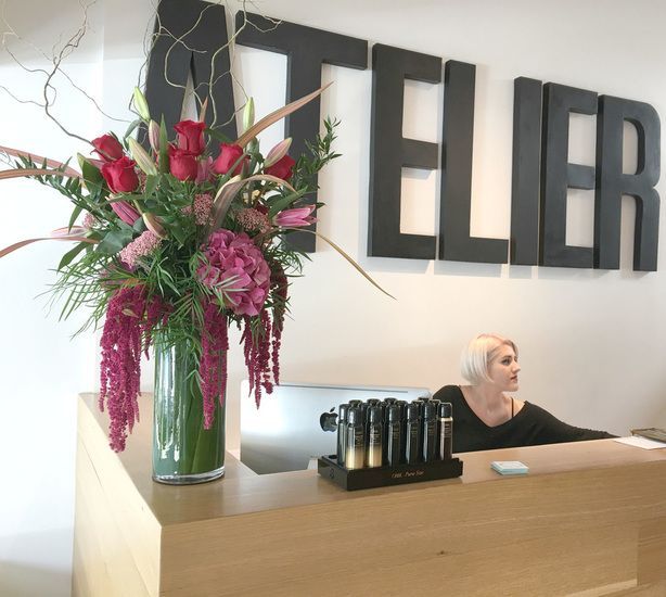 A woman sits at a desk in front of a sign that says atelier