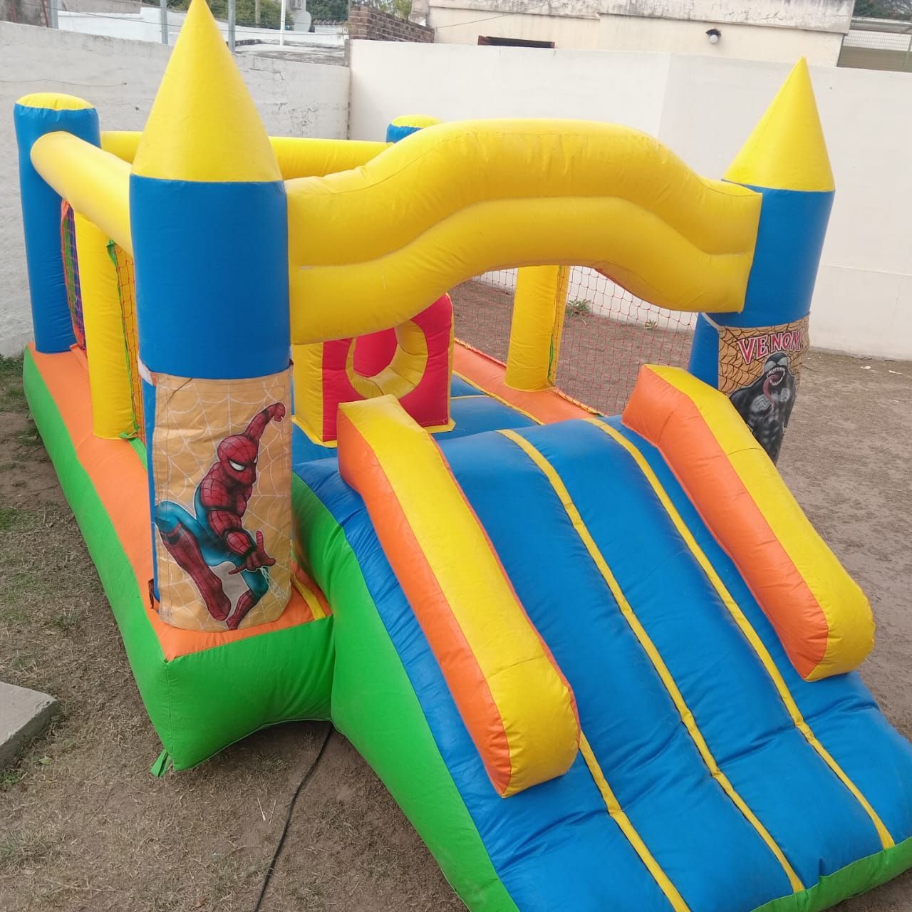 Castillo hinchable colorido con tobogán azul, amarillo y verde para exteriores.