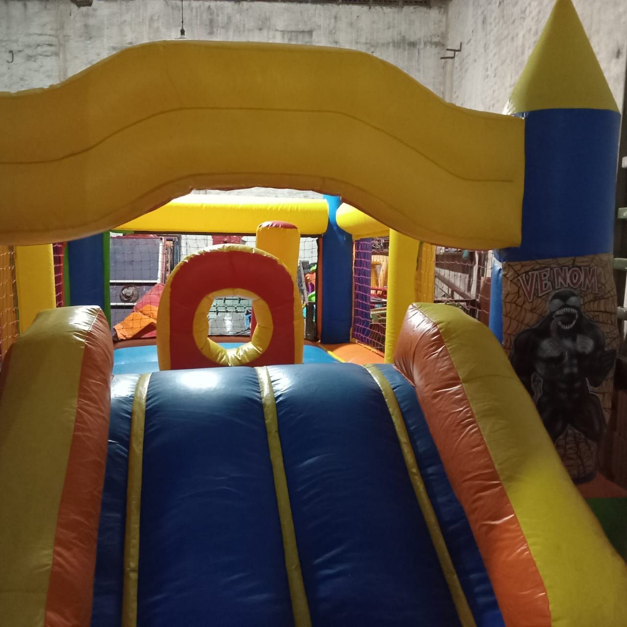 Castillo hinchable colorido con tobogán azul y arco amarillo en un área de juegos interior.