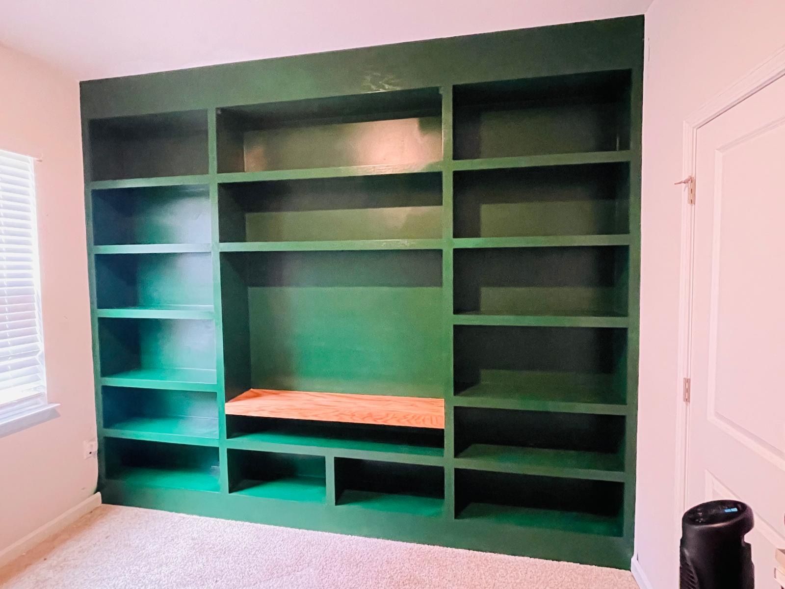 A room with green shelves and a wooden bench.