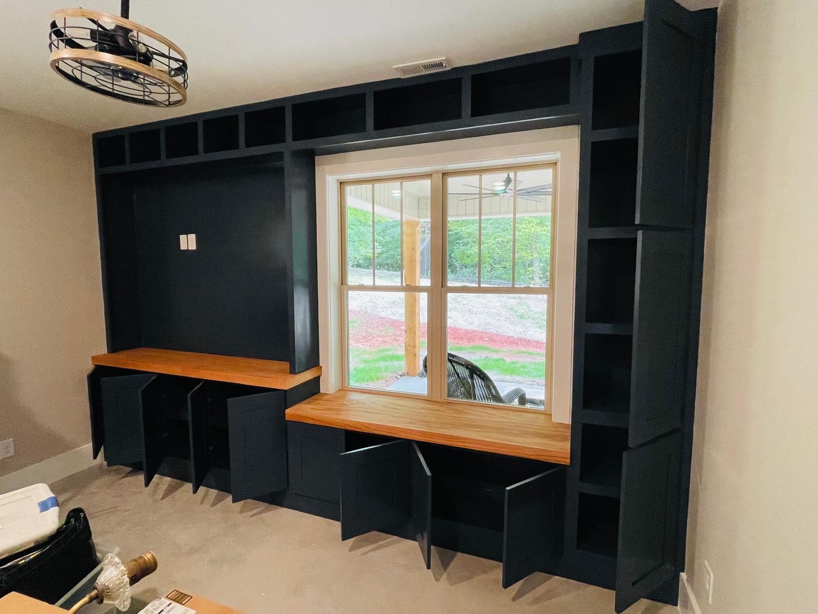 A room with a window , a desk , shelves and a fan.