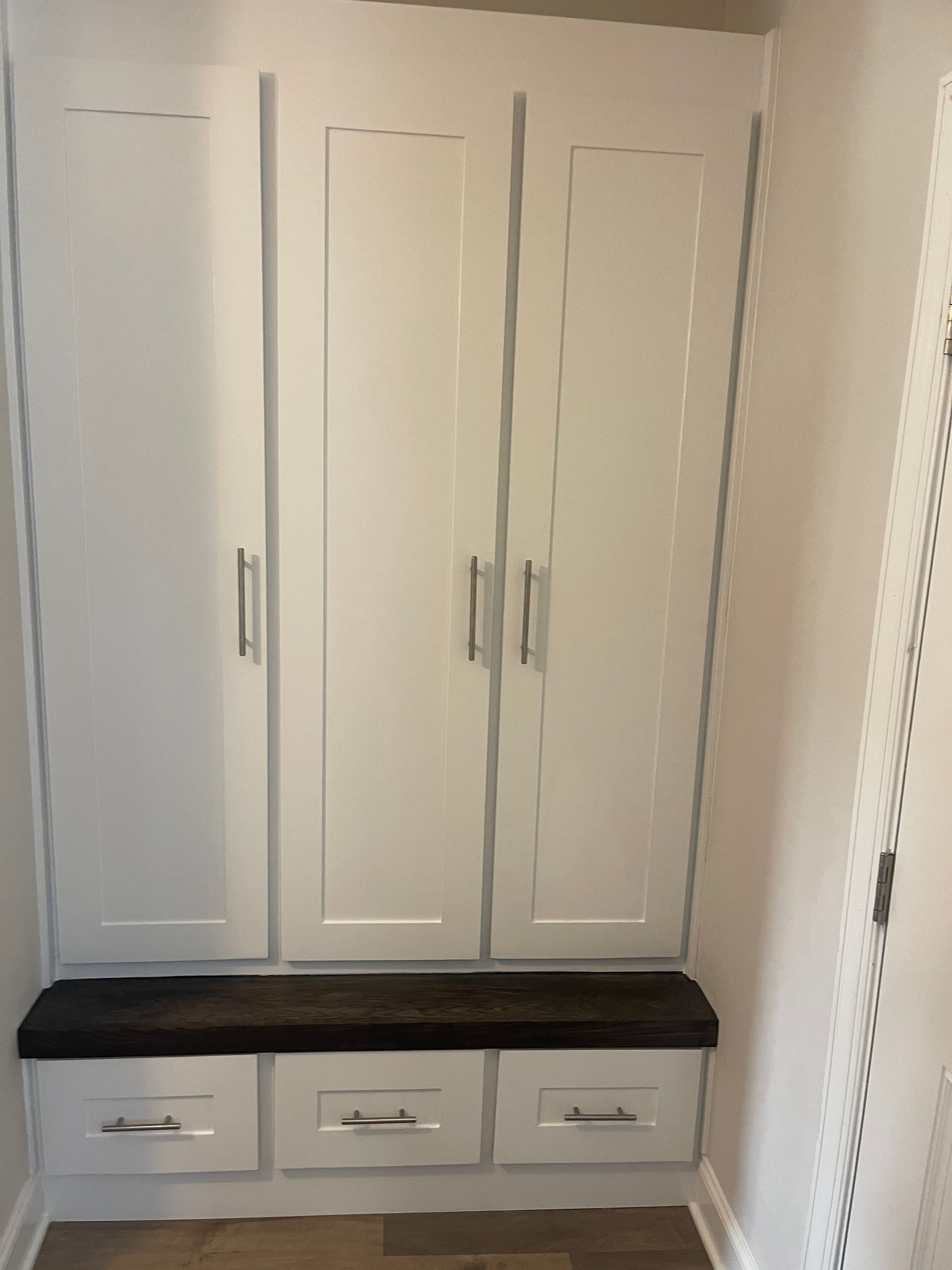A room with white cabinets and drawers and a bench.