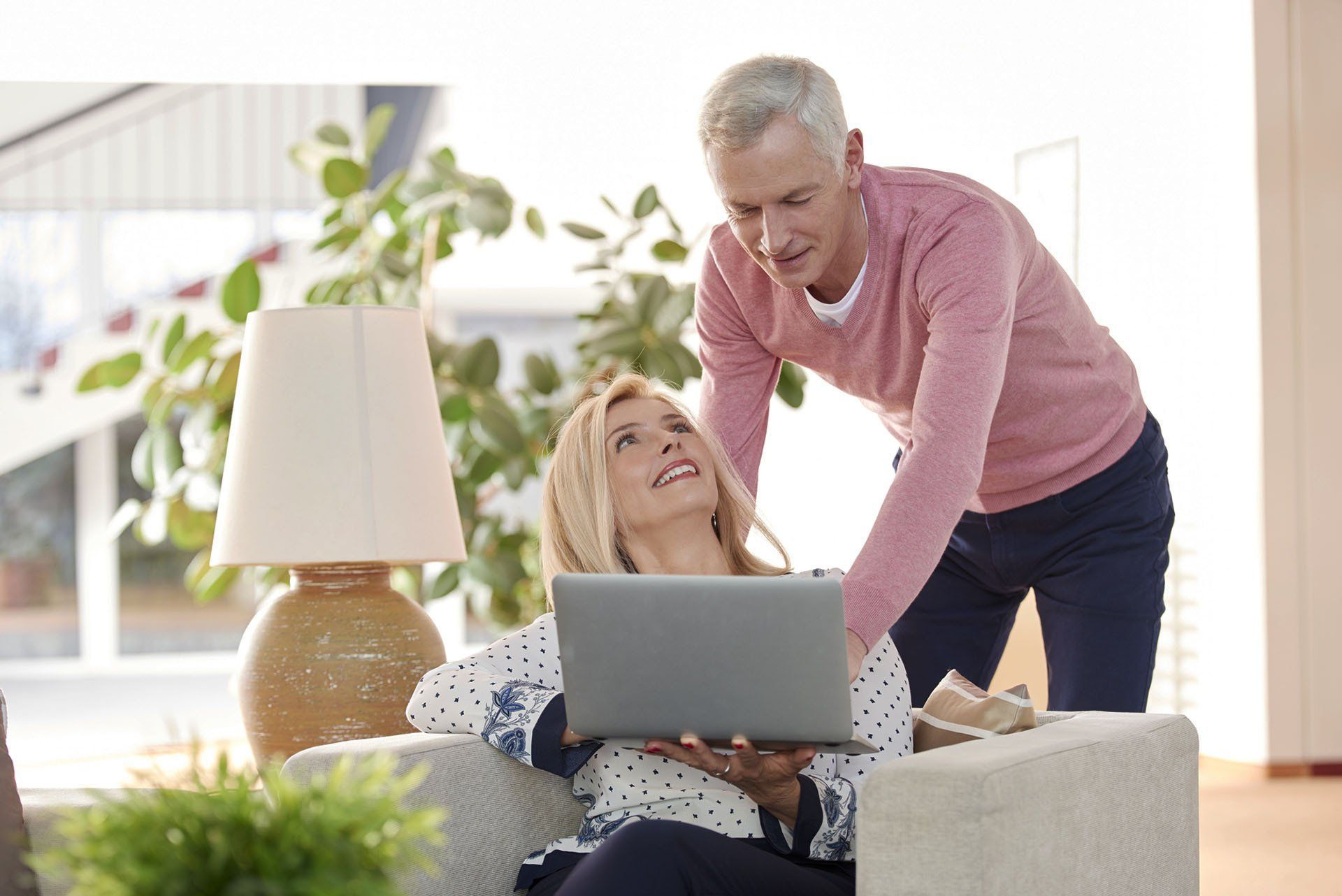 A couple looks at a laptop screen together in a bright, modern living room.